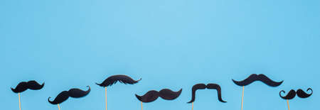 Various black photo booth props moustaches of different shape on blue background. Greeting card for father's day or men's health awareness month campaign concept. Flat lay, banner.の写真素材