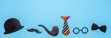 Various black photo booth props: cylinder hat, glasses, moustache, smoking pipe, bow tie on blue background. Greeting card for father's day, masculinity concept. Flat lay, copy space, mock up, banner.の写真素材