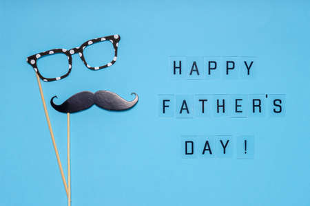 Photo booth props moustache and glasses on blue background. Text HAPPY FATHER'S DAY, greeting card in minimal style. Flat lay.の写真素材