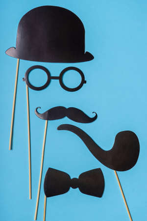 Various black photo booth props: cylinder hat, glasses, moustache, smoking pipe, bow tie on blue...