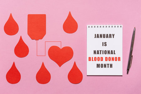 Text JANUARY IS NATIONAL BLOOD DONOR MONTH on white notebook page with red drops on pink background. Annual national red cross campaign in January, 2021. Charity, donation, volunteer concept.の写真素材
