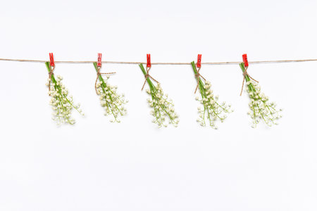 Creative spring composition with small bouquets of lilies of the valley flowers hanging on rope by clothespins on white background. Springtime concept, mock up for greeting card, copy space.の写真素材