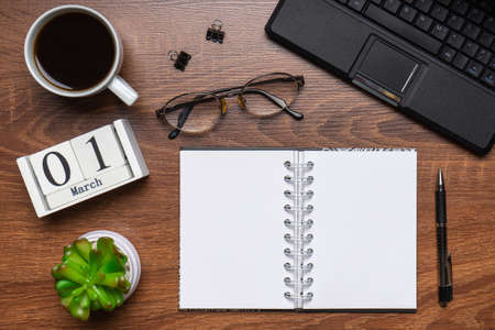 Modern office workplace with laptop keyboard, coffee cup, smart phone, stationery and plant. Date 01 March on wooden block calendar. White empty notepad page. Table top view, flat lay, copy spaceの写真素材