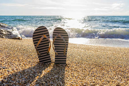 Flip-flops on sea beach against sunny seascape. Flip flops slippers in nautical style in small...