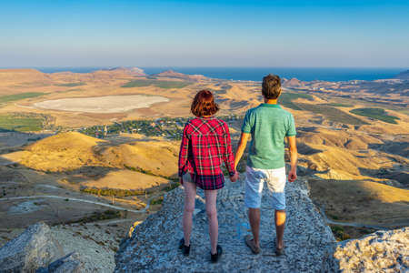 Rear view of family couple standing on mountain cliff and admiring beautiful landscape of coastal...