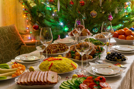 Festive Christmas served table against beautiful green pine tree decorated with many colorful new year toys. Xmas dinner, delicious food, christmas turkey. Winter holidays celebration at cozy home.の写真素材