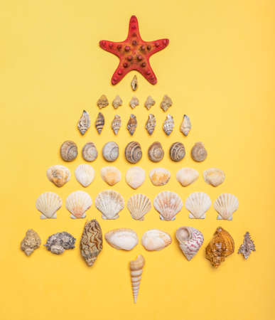 Christmas tree made of decorative sea shells and seastar on pastel yellow background. Christmas or New Year holidays at sea. Winter vacation or weekend at ocean concept. Sea travel, cruise, voyage.の写真素材