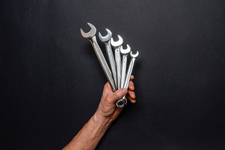 Men's hand holding set of wrenches on black background. Tools in human hand. Man worker with spanners. Technique repair, equipment for mechanical service, labor or father's day concept. top view.の写真素材