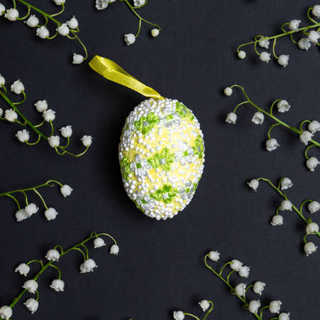Easter composition with decorative easter egg and fresh white lilies of the valley flowers on black background. Happy Easter concept, greeting card. Flat lay, top view.の写真素材