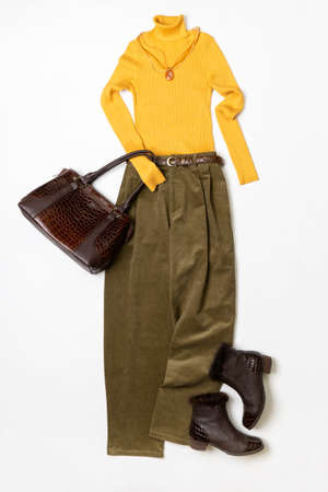 Female spring or autumn stylish clothing set. Yellow sweater and leather boots, green corduroy trousers, handbag. Trendy fashionable casual clothes. fashion concept.の写真素材