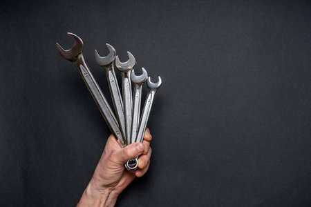 Men's hand holding set of wrenches on black background. Tools in human hand. Man worker with spanners. Technique repair, equipment for mechanical service, labor or father's day concept.の写真素材
