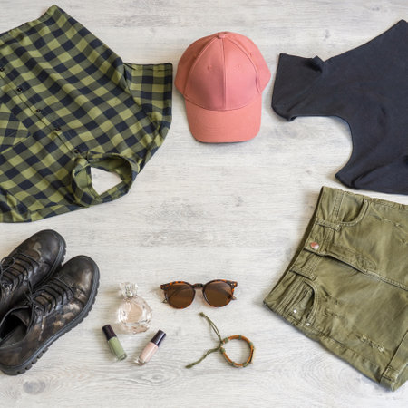 Stylish women's or teenager's clothing set with accessories: checkered shirt, jersey top, jeans shorts, cap, backpack, sunglasses, bracelet, perfume, boots. Summer female outfit, copy space.の写真素材