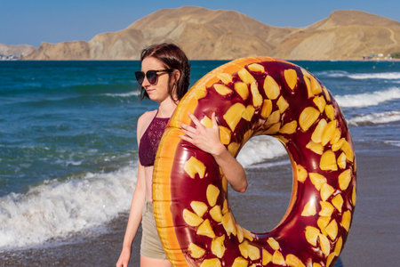 Teen girl with donut lilo against summer landscape of sea and mountains in sunny day. Beautiful...