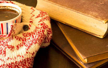 Cup of black coffee in warm scarf and old booksの写真素材