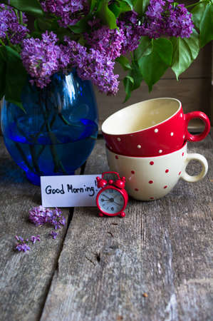 Lilac flowers in a vase and tea cups on the old wooden tableの写真素材