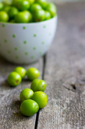 Cup with green plums and daisy flowers in a vase on old tableの写真素材