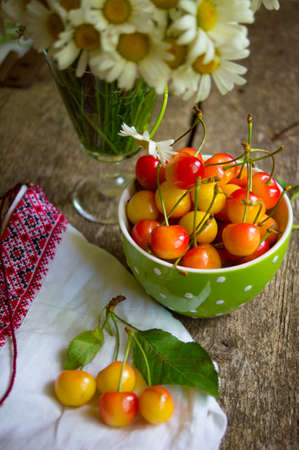 Daisy flowers in a vase and sweet cherries on the tableの写真素材