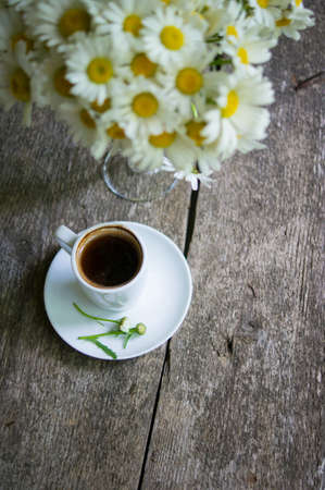 Cup of black coffee and daisy flowers on the old tableの写真素材