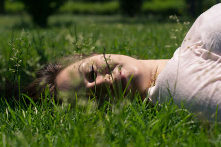 Portrait of young beautiful woman lying in green summer fieldの写真素材