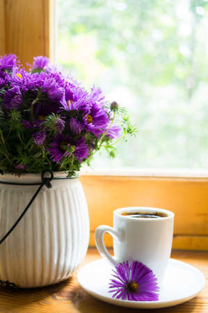 Cup of coffee and aster flowers in a vase on the wooden windowの写真素材