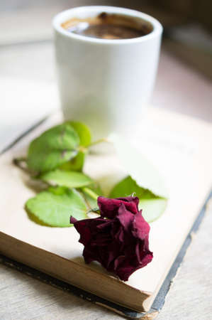 Cup of coffee, old book and dry red rose on the tableの写真素材