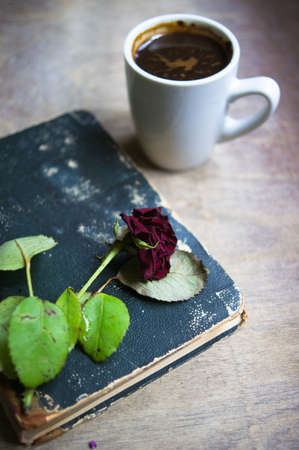 Cup of coffee, old book and dry red rose on the tableの写真素材
