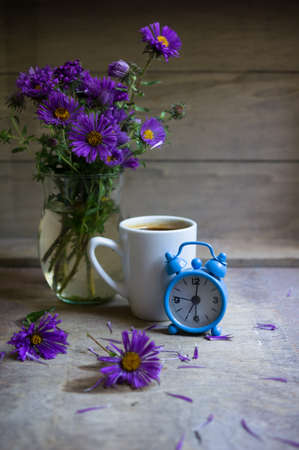 Cup of coffee and aster flowers in a vase on the wooden table