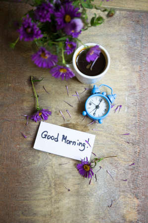 Cup of coffee and aster flowers in a vase on the wooden table