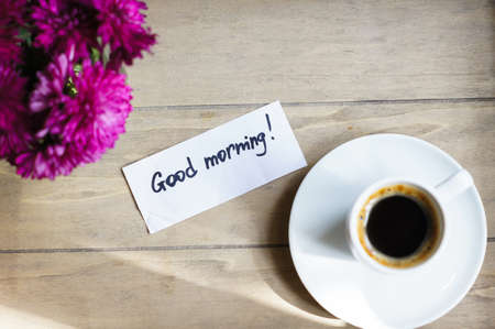 Cup of coffee, note and flowers on the old wooden tableの写真素材