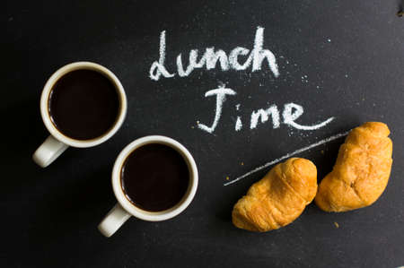 Cup of black coffee and croissants on the chalkboard with noteの写真素材