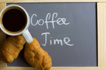Cup of black coffee and croissants on the chalkboard with coffee time noteの写真素材