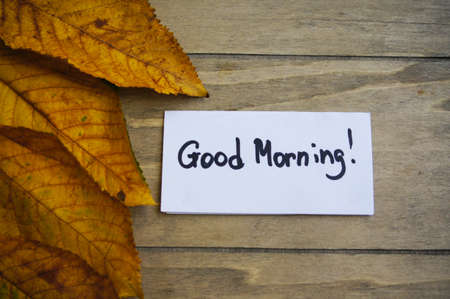 Yellow autumnal leave and Good morning note on the wooden tableの写真素材