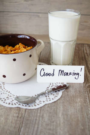 nutritious cereal cornflakes breakfast on the wooden table with good morning note and milkの写真素材