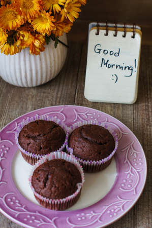 Chocolate cupcakes, good morning note and flowers on a tableの写真素材