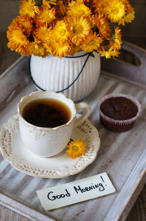 Chocolate cupcakes, cup of tea, good morning note and flowers on a table