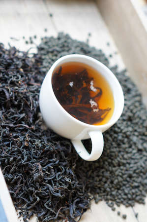 Cup of tea surrouded dry tea leaveas