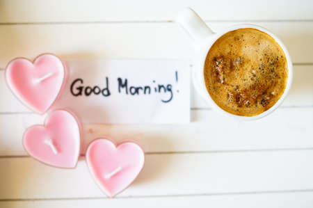 Cup of coffee and red cloves flowers in a vase with good morning noteの写真素材