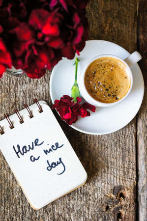 Cup of coffee and red cloves flowers in a vase with good morning noteの写真素材