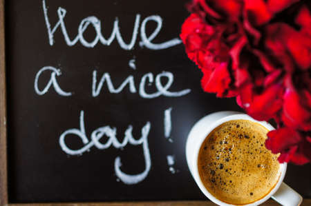 Cup of coffee and red cloves flowers in a vase with good morning noteの写真素材