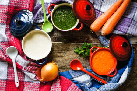 Different kinds of soups - sprinach soup, french onion cream-soup and carrot cream-soup on the tableの写真素材