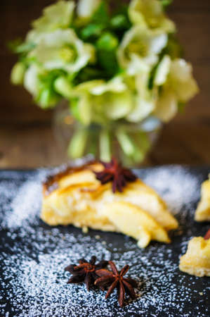 French apple tart on the old rustic table with flowers and napkin
