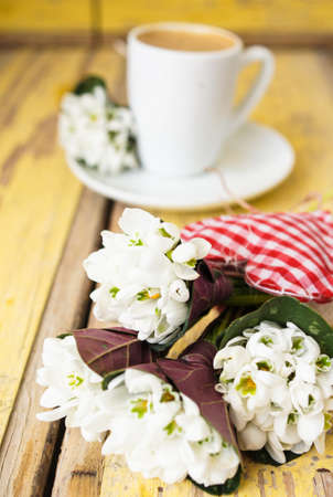 Cup of black coffee and first spring snowdrop flowers on the old table