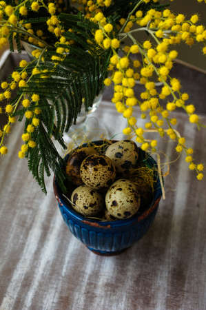Easter time, Hand decorated Easter Eggs and speckled birds eggs in straw with a branch of colorful yellow clusters of mimosa flowers in a natural country Easter backgroundの写真素材