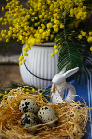 Easter time, Hand decorated Easter Eggs and speckled birds eggs in straw with a branch of colorful yellow clusters of mimosa flowers in a natural country Easter backgroundの写真素材