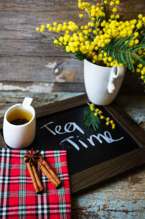 Glass cup with tea and blooming yellow mimosa with good morning note on wooden backgroundの写真素材