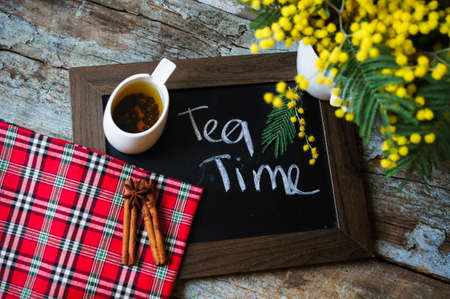 Glass cup with tea and blooming yellow mimosa with good morning note on wooden backgroundの写真素材