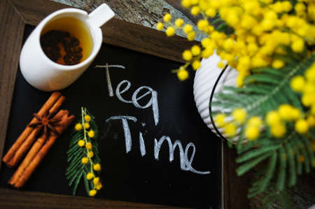 Glass cup with tea and blooming yellow mimosa with good morning note on wooden backgroundの写真素材