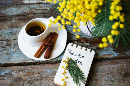 Glass cup with tea and blooming yellow mimosa with good morning note on wooden backgroundの写真素材