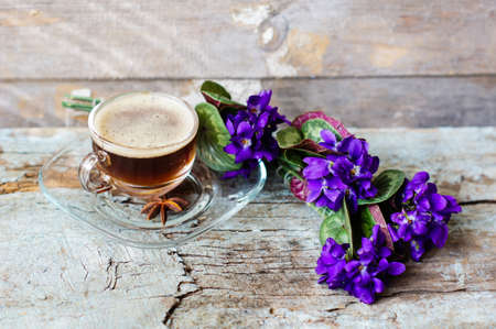 First spring flowers of violets and cup of coffee on the old wooden table