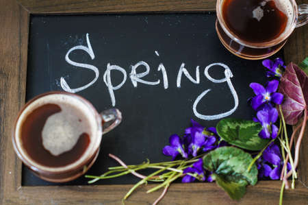 First spring flowers of violets and cup of coffee on the old wooden table